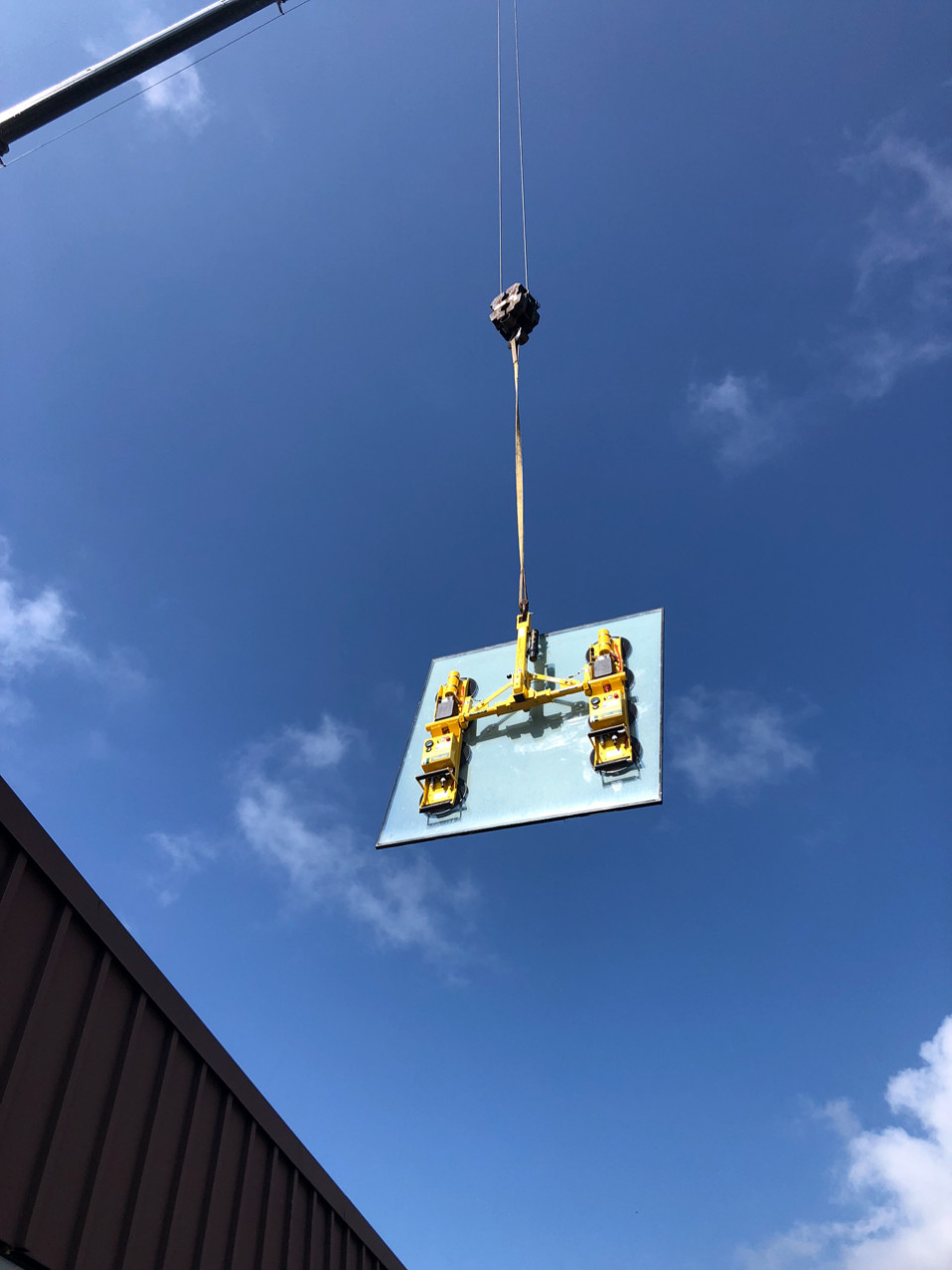 Power cup vacuum lifting system hangs from a crane to install heavy glass units.